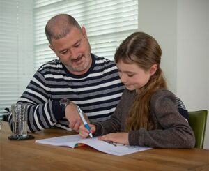 vader en dochter met oefenboek aan tafel